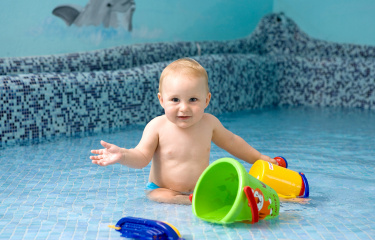 Baby spielt im flachen Wasser mit Eimern und Booten