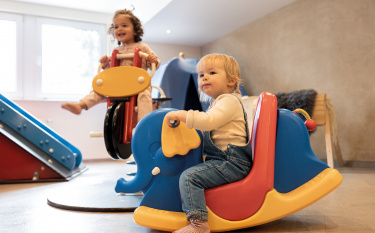 Zwei Kleinkinder sitzen jeweils auf einer Federwippe in der Spiellounge