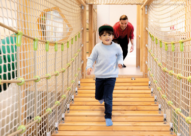 Junge läuft über Hängebrücke, Betreuer im Hintergrund 