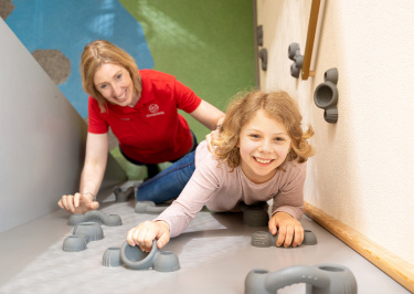 Betreuerin hilft Mädchen beim Klettern an einer Kletterwand