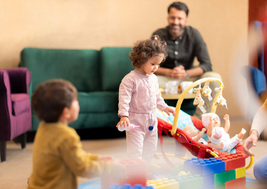 Vater auf dem Sofa beobachtet seine kleinen Kinder beim Spielen