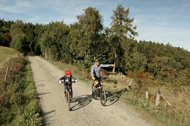 Vater und Kind radeln über einen ruhigen Waldweg.