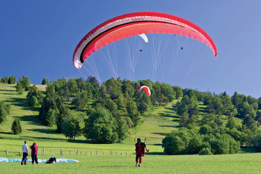 Ein Gleitschirmflieger schwebt sanft über eine grüne Wiese dem Boden entgegen.