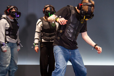 Drei Personen mit Virtual-Reality-Brillen und Spezialwesten bewegen sich konzentriert durch einen Raum.