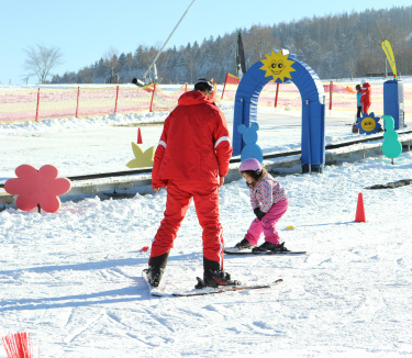 Skilehrer begleitet Kind im Anfängerbereich mit bunten Figuren.